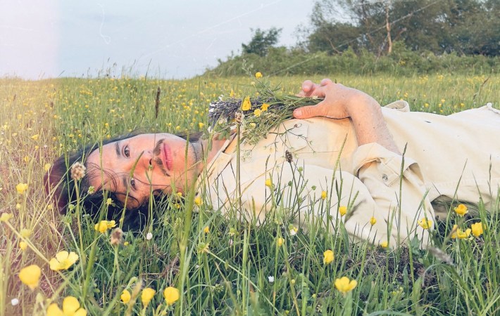 Portrait of Welsh singer/songwriter Tom Jenkins, laying in a blooming field looking directly in the camera, inviting the viewer to listen to his new EP.